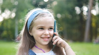 Mutlu küçük kız yaz parkında cep telefonuyla konuşuyor..
