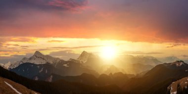 Yüksek tepeleri ve sisli vadisiyle gün batımı manzarası kayalık dağlarda canlı bir akşam gökyüzü altında.