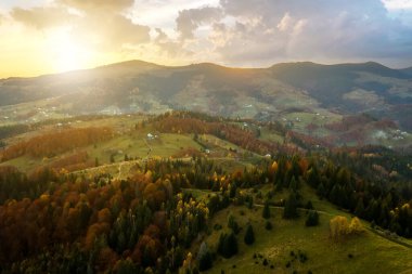 Ukrayna 'nın Karpat Dağları' ndaki sonbahar ormanları arasındaki geniş tepelerde küçük çoban evleri olan uzak köyün hava manzarası gün batımında.