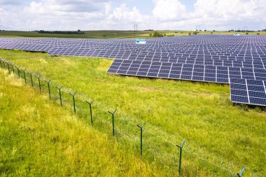 Yeşil alandaki güneş enerjisi santralinin koruyucu tel örgülü havadan görüntüsü. Temiz ekolojik enerji üretmek için elektrik panelleri.