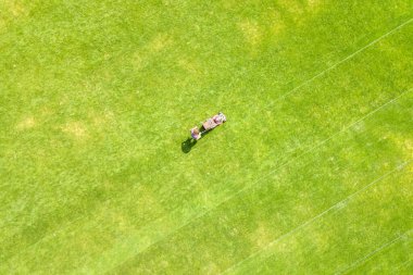 Yazın futbol sahasında çimenleri biçen ve çim biçen küçük işçi figürünün havadan görünüşü..