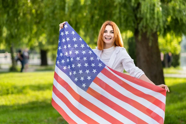 Portret Szczęśliwej Młodej Rudowłosej Kobiety Trzymającej Flagę Usa Rękach Stojącej — Zdjęcie stockowe