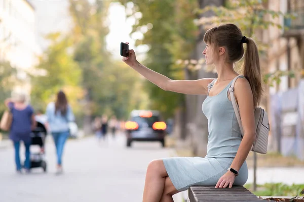 여자가 여름날 야외에 도시의 의자에 전화로 셀카를 — 스톡 사진