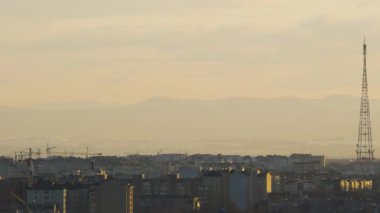 Yüksek binaları olan şehir manzarası yapım aşamasında ve yüksek dağ siluetlerine karşı kule vinçleri hareket ediyor.