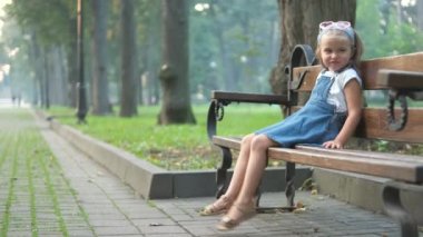 Küçük mutlu bir kız çocuğu yaz parkında bir bankta dinleniyor..