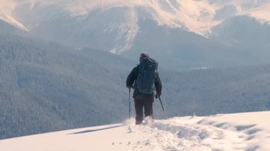 Sırt çantalı bir adam soğuk kış gününde dağ yamacında yürüyüş yapıyor..