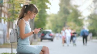 Genç meşgul bir kadın sıcak bir yaz gününde şehir bankında cep telefonuyla konuşuyor..