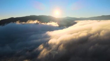 Gün batımında dağ tepelerini ve köy evlerini kaplayan karamsar sis bulutlarının hava manzarası.