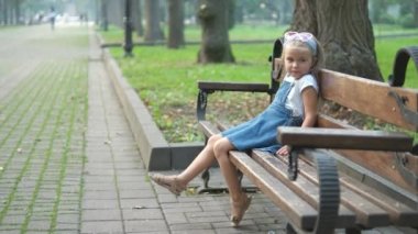 Küçük mutlu bir kız çocuğu yaz parkında bir bankta dinleniyor..