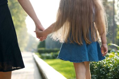 Anne ve uzun saçlı küçük kızı yaz parkında el ele yürüyorlar..