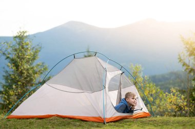 Yürüyüşçü çocuk kamp alanında kamp çadırında dinleniyor yaz manzarasının tadını çıkarıyor..