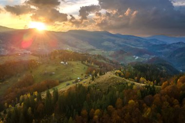 Günbatımında Ukrayna Karpatlar 'daki sonbahar ormanları arasında geniş çayırlardaki küçük çoban evlerinin havadan görünüşü.