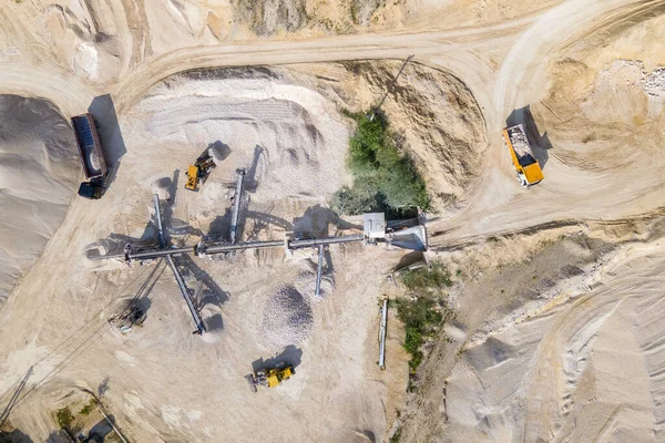 Open pit mining of construction sand stone materials with excavators and dump trucks at conveyor belt.