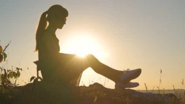Siyah kısa elbiseli genç, sıska bir kadın yaz günbatımında bir kayanın üzerinde oturmuş dinleniyor. Modaya uygun bir kadın doğada sıcak bir akşamın tadını çıkarıyor..