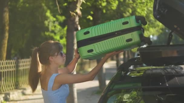 車の屋根のラックから緑のスーツケースを取り出し 街の通りを歩く若い女性観光客 旅行と休暇のコンセプト — ストック動画