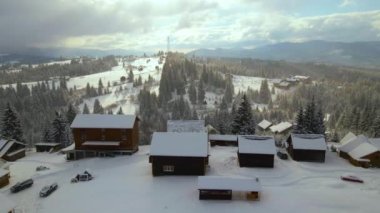Çorak dağ manzarası. Kışın karanlık ormanlar arasında kırsal evlerin üzerine düşen karlar..