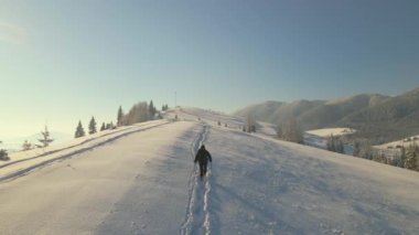 Sırt çantalı bir yürüyüşçü soğuk kış gününde karlı dağ yamacında yürüyor..