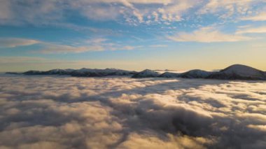 Ufuktaki Karpat dağlarının uzak karanlık zirveleriyle beyaz yoğun sis üzerinde canlı gün doğumunun havadan görüntüsü.