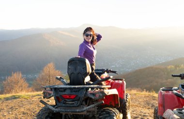 Genç, mutlu kadın sürücü günbatımında ATV dörtlü motosiklet sürüşünün keyfini çıkarıyor..