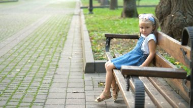 Küçük mutlu bir kız çocuğu yaz parkında bir bankta dinleniyor..