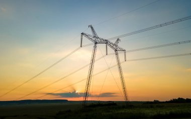 Güneş doğarken elektrik hatları olan yüksek voltajlı kulelerin koyu gölgesi..