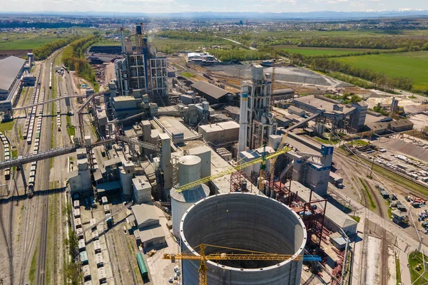 Aerial view of cement factory with high concrete structure and tower crane at industrial production area. Manufacture and global industry concept.