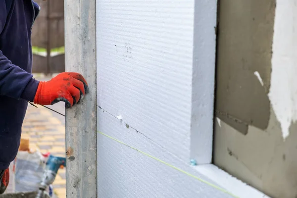 Construction worker installing styrofoam insulation sheets on house facade wall for thermal protection.