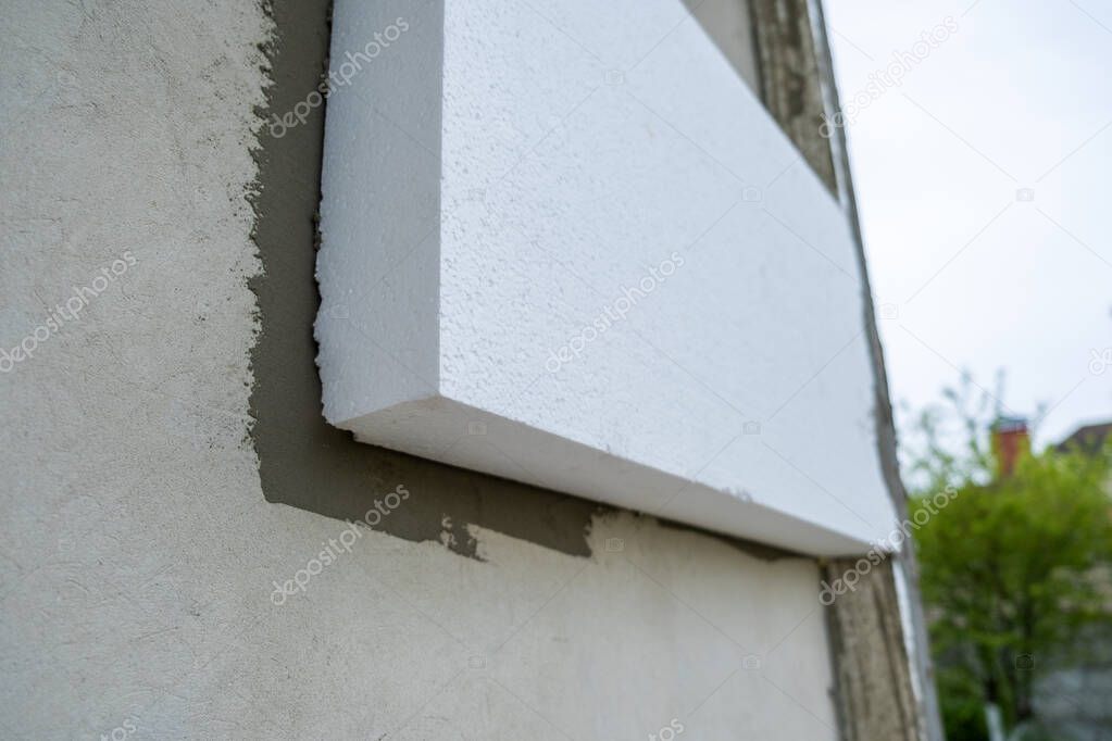 Installation of styrofoam insulation sheets on house facade wall for thermal protection.