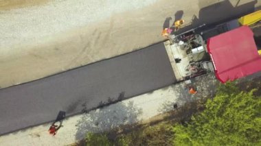 Çalışan işçiler ve asfalt döşeyen makinelerle yeni yol yapımının havadan görünüşü.