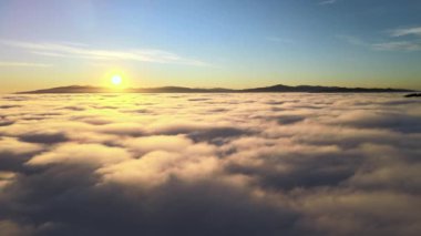 Ufuktaki uzak dağlarla beyaz kabarık bulutların üzerinde sarı günbatımının havadan görünüşü.