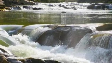 Berrak turkuaz suyu olan dağ nehri, kalın beyaz köpüklü ıslak kayaların arasına dökülüyor..