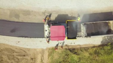 Çalışan işçiler ve asfalt döşeyen makinelerle yeni yol yapımının havadan görünüşü.