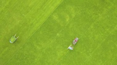 Yazın futbol sahasında çimenleri biçen ve çim biçen küçük işçi figürünün havadan görünüşü..