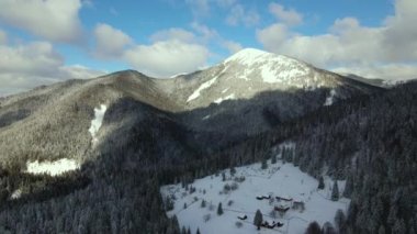 Soğuk dağlarda karla kaplı ormanlar arasında küçük kır evleri olan hava manzarası.