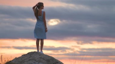 Yazın gün batımının tadını çıkaran bir taşın üzerinde duran genç bir kadının karanlık silueti..