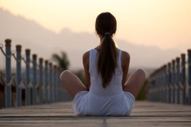 Açık renk elbiseli genç bir kadın deniz kıyısında güneşli bir sabahta dinleniyor. Yaz tatili ve seyahat konsepti.