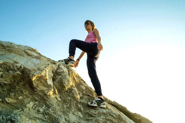 Woman hiker climbing steep big rock on a sunny day. Young female climber overcomes difficult climbing route. Active recreation in nature concept.