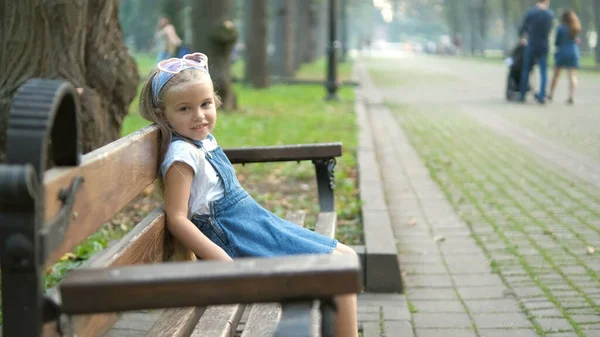 Küçük Mutlu Bir Kız Çocuğu Yaz Parkında Bir Bankta Dinleniyor — Stok fotoğraf