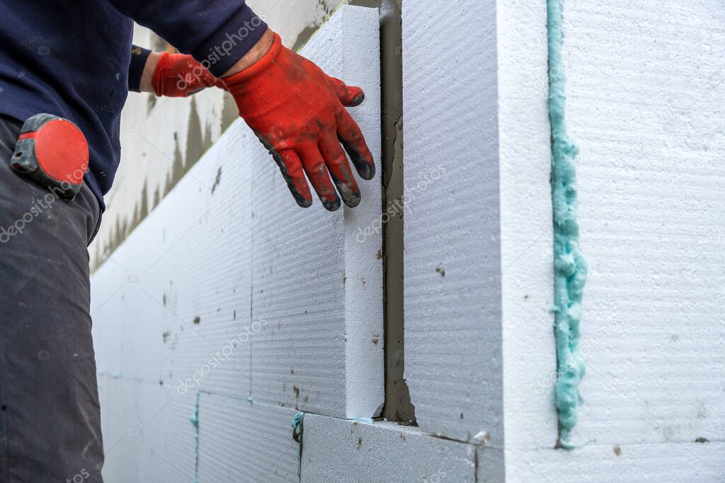 Construction worker installing styrofoam insulation sheets on house facade wall for thermal protection.