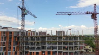 İnşaat halindeki yüksek beton binadaki vinçler ve profesyonel işçiler. Gayrimenkul geliştirme kavramı.