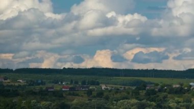 Kırsal alandaki küçük evlerin üzerinde mavi gökyüzünde hızla ilerleyen beyaz kabarık kümülüs bulutlarının hızlandırılmış görüntüleri.