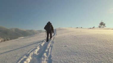 Sırt çantalı bir yürüyüşçü soğuk kış gününde karlı dağ yamacında yürüyor..