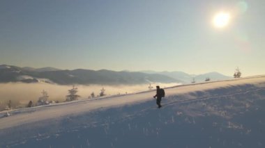 Sırt çantalı bir yürüyüşçü soğuk kış gününde karlı dağ yamacında yürüyor..