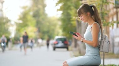 Sıcak yaz gününde cep telefonuyla mesajlaşan genç ve güzel bir kadın açık hava bankında oturuyor..