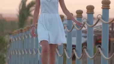 Akşamları sahilde uzun bir rıhtımda yürüyüşe çıkan beyaz elbiseli genç bir kadın. Tatil ve seyahat kavramı.
