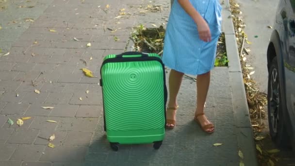 若い女性ドライバーは街の通りの車から緑のスーツケースを取り出します 旅行と休暇のコンセプト — ストック動画
