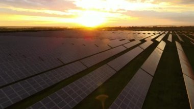 Günbatımında temiz ekolojik elektrik enerjisi üretmek için sıra sıra güneş fotovoltaik panelleri olan sürdürülebilir büyük elektrik santralinin havadan görünüşü. Sıfır emisyon kavramı ile yenilenebilir elektrik.