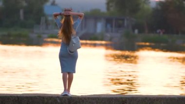 Sıcak bir akşamda göl kenarında rahatlayan günlük kıyafetli genç bir kadın. Yaz tatilleri ve seyahat konsepti.