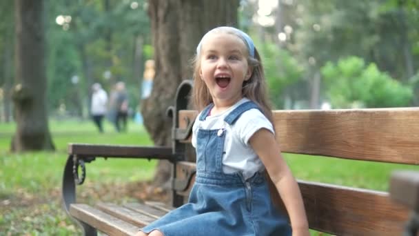Kleines Glückliches Kindermädchen Sitzt Auf Einer Bank Und Lächelt Glücklich — Stockvideo