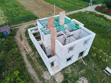 Havalandırılmış hafif beton duvarları ve inşaat halindeki ahşap çatı kirişleri olan bitmemiş özel evin havadan görüntüsü..